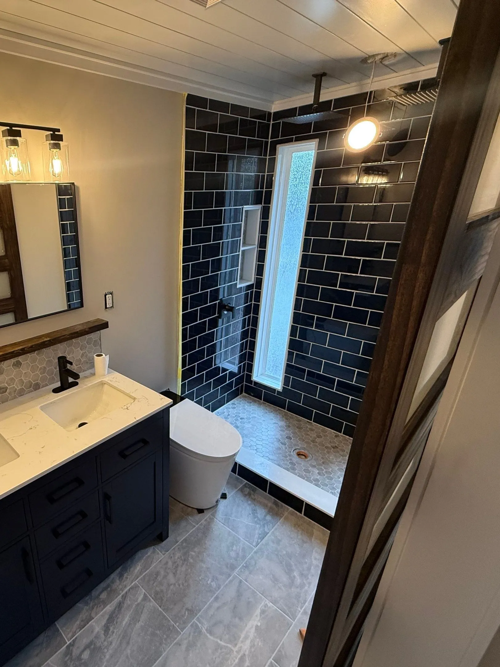 Remodeled bathroom with a navy subway-tile walk-in shower and hex tile floor
