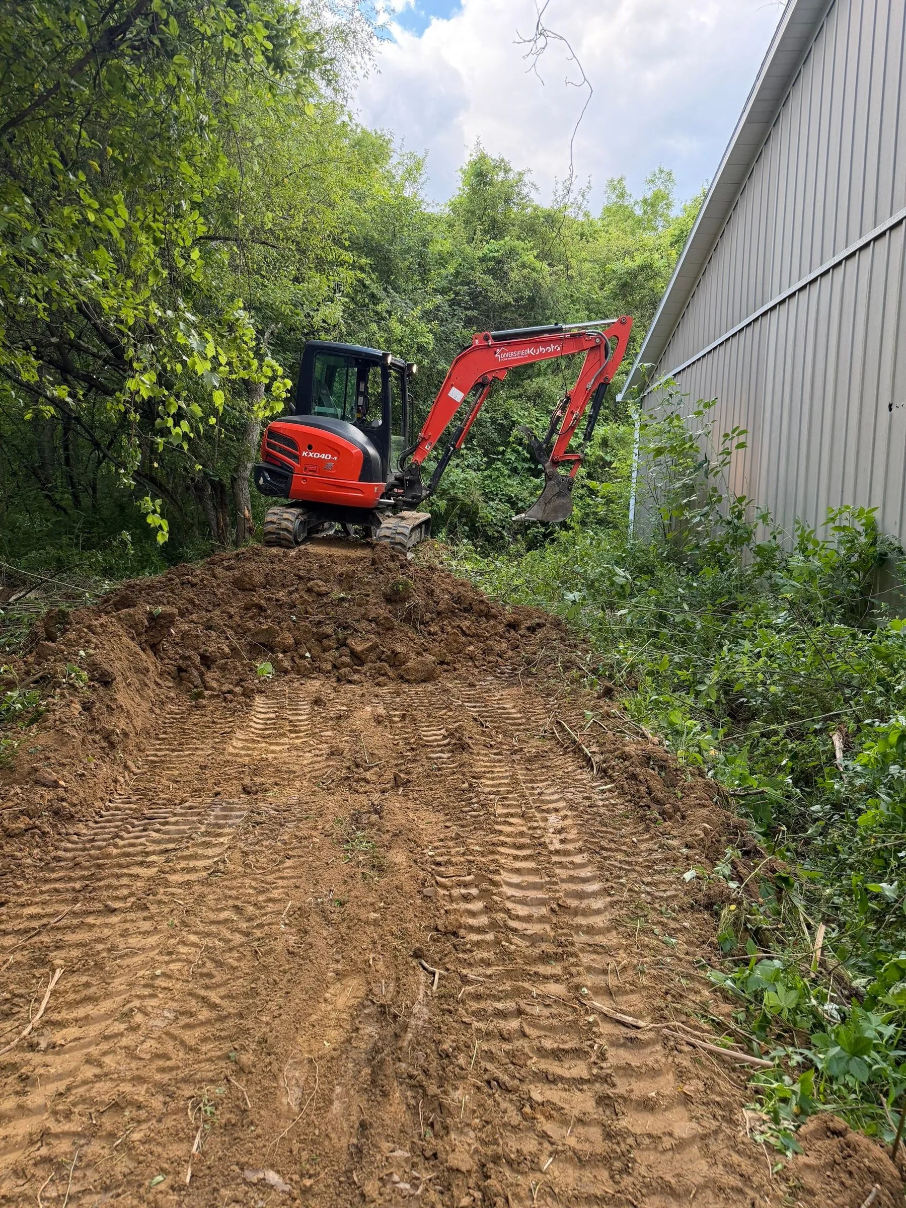 DHI mini excavator clearing a path beside a building