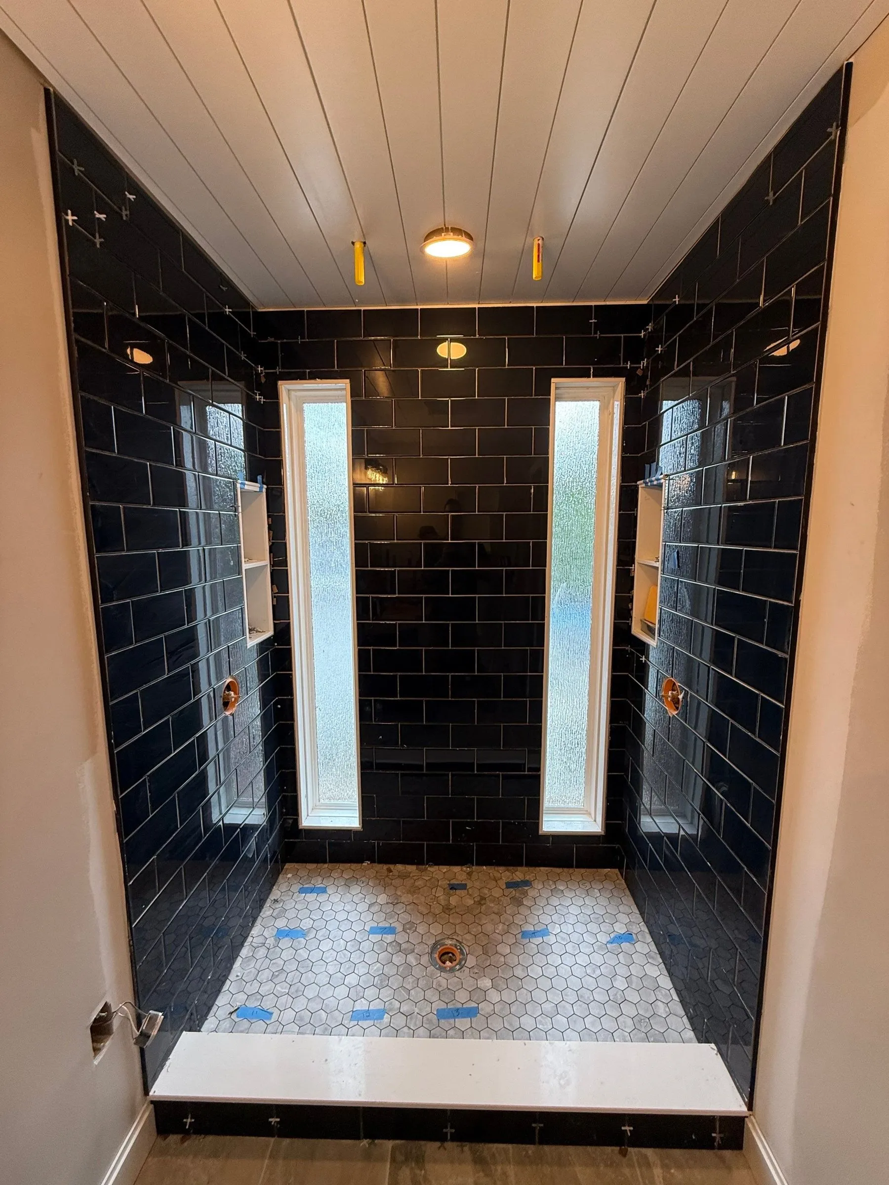 Walk-in shower with navy subway tile, hex tile floor and two tall frosted windows