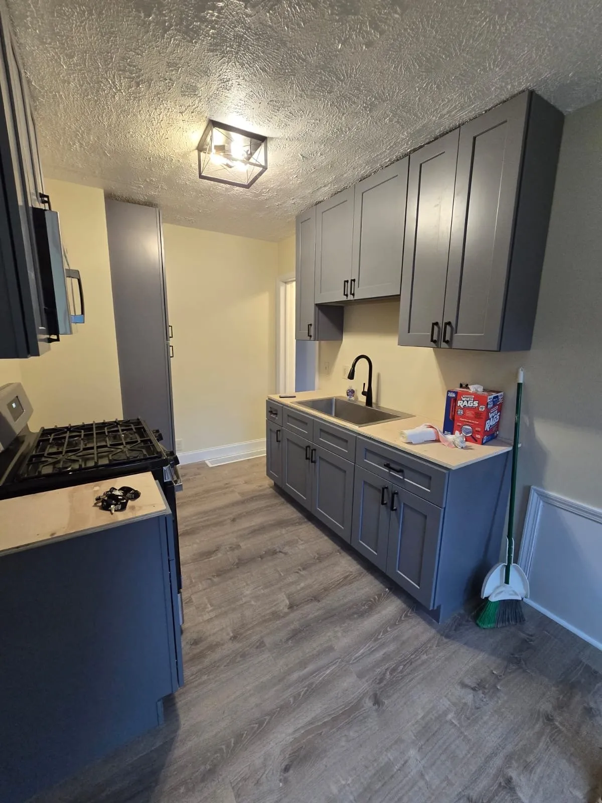 Galley kitchen with new gray shaker cabinets, black hardware and vinyl plank floor